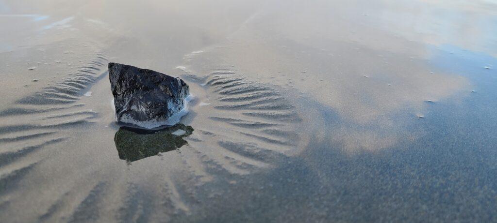 A smooth stone resting in quiet wet sand.